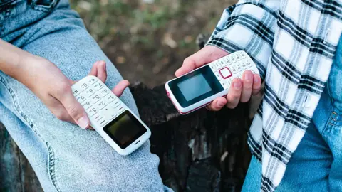 Getty Images Small push-button mobile phones pictured in the hands of teenagers outdoors