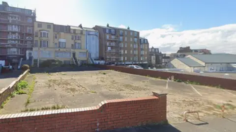 A derelict building with an empty car park in front of it
