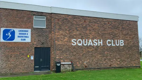 A brick building with the words "squash club" written on the side in white lettering