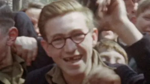 Yorkshire & North East Film Archive A young Bill Gilchrist. He has his light hair combed back and is wearing round-rimmed glasses. He is smiling at the camera, revealing a missing front tooth.