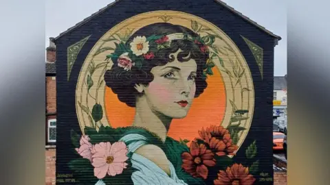 Art Friends Warwickshire A mural of a woman's face surrounded by flowers on a building