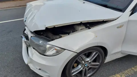 @roadpoliceBCH Part of the front passenger side of a white BMW car shows damage to the bonnet and the bumper