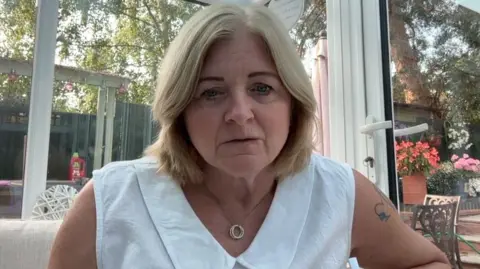 Debbie Adlam has blonde hair and wears a white top.