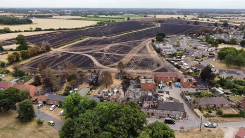 Shaun Whitmore/BBC An aerial image of a village showing a large field which is scorched black and homes wrecked by fire 