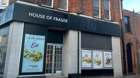 Archive photograph of the former House of Fraser store in Victoria Street, There are posters in the window advertising food with the slogan shop, drop, eat.