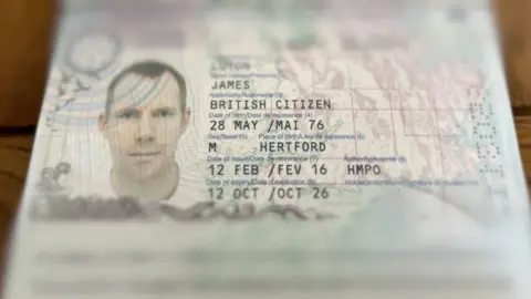 Tony Fisher/BBC Close-up of an open British passport showing a photo ID page with a portrait illustration and printed personal details, with the page edges slightly out of focus.