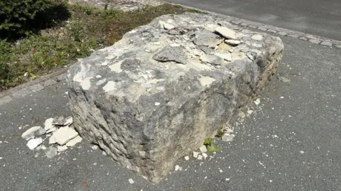 A large rectangular boulder on a path. Fragments of chipped rock are on top and next to it.