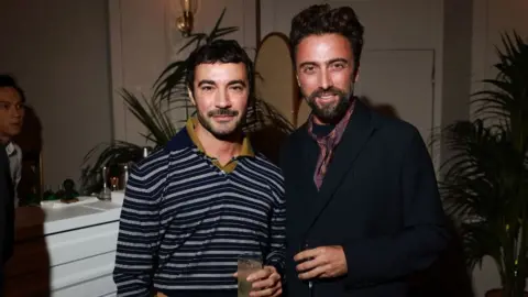 Getty Images Dario Vitale pictured with a friend, he is wearing a blue and grey striped shirt and holding a drink.