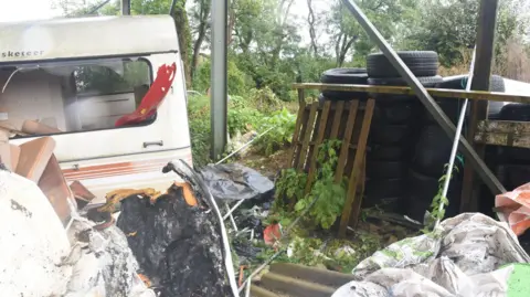 Avon and Somerset Police The site where Michael Wheeler's remains were found, with an old-fashioned white caravan on the left and various bits of wood and plastic packaging strewn around