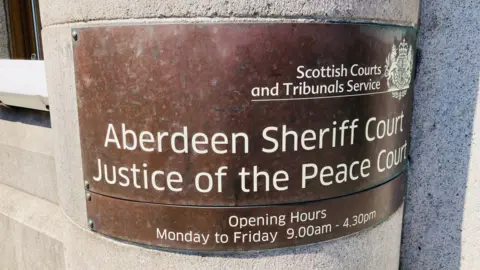 Bronze curved sign saying Aberdeen Sheriff Court Justice of the Peace Court on a granite wall. 