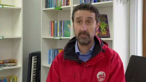 BBC Steve Hitchcock, head teacher of St Peter's Church of England Primary School in Budleigh Salterton sitting in the school libary