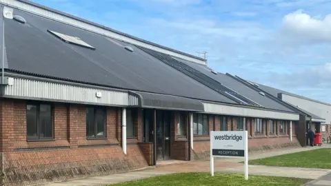 A sign next to a large industrial building says 'westbridge reception'.
