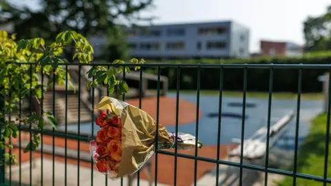 Getty Images A bouquet of flowers is put into a fence overlooking a school building and grounds