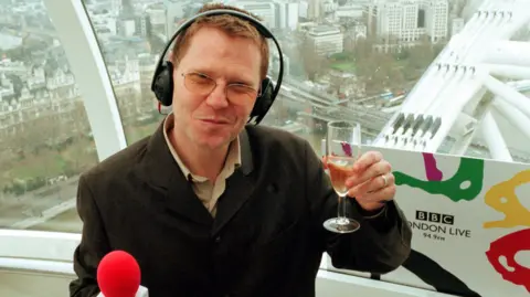Robert Elms photographed several years ago holding a glass of champagne with headphone on his head while travelling on the London Eye