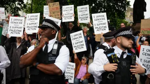 Police standing in front of protesters holding placards in support of Palestine Action