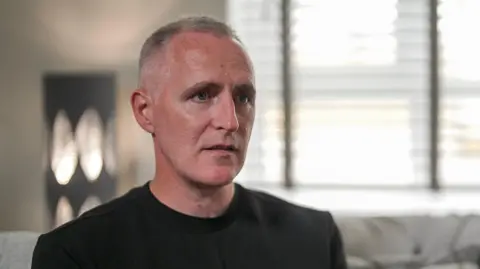 Gerry, who wears a black T-shirt and has short grey hair, speaks to the BBC in his home. 