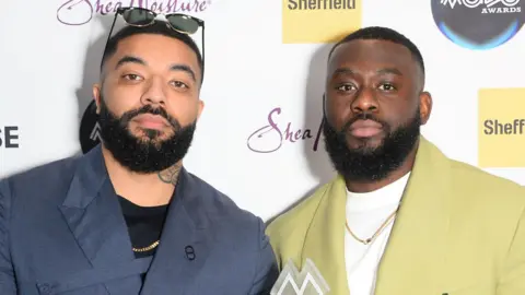 Getty Images James Duncan and Fuhad Dawodu at the MOBO Awards in Sheffield in February 2024. Both men have short afro hair and beards and look seriously at the camera. James weards a dark blue shirt over a black top and has sunglasses perched on his head. Fuhad wears a pale green suit over a white top. 