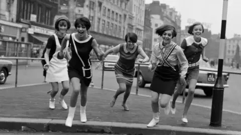 Getty Images Black and white image Mary Quant (middle/dead centre of the girls) and four models running in the street.