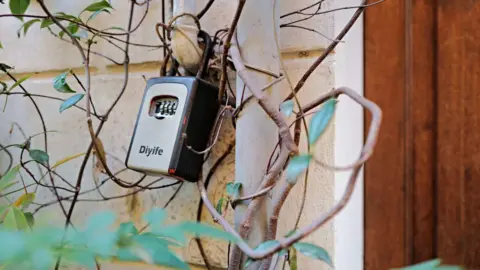 A key box - a lock mechanism padlocked to a building - next to a door in Italy.