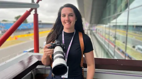 Kris Holland/BBC A woman holding a camera with a telephoto lens