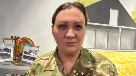 Sgt Adams wears army clothing and looks off to the right of the camera. She has short hair.