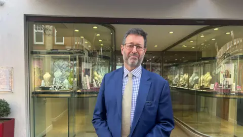 BBC A man in a suit stood outside the front of a jewellery store