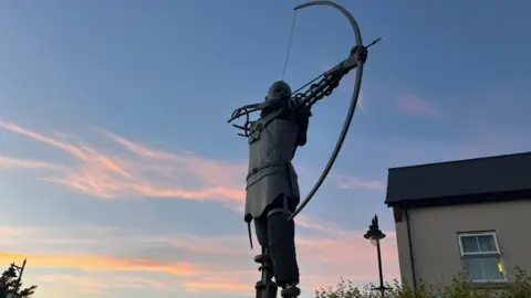 Weather Watchers/Runner A silhouette of an archer statue shooting a bow and arrow.