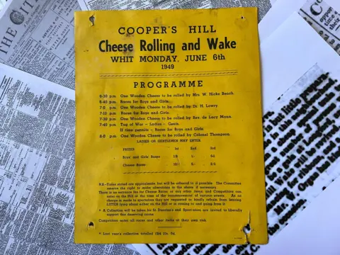 Jean Jefferies Collection A yellowed 1949 programme poster for the Cooper’s Hill Cheese Rolling and Wake in Gloucestershire, listing the event schedule, races and prizes, laid on top of old newspaper pages.