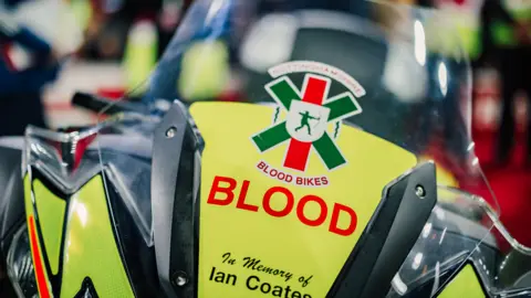 Nottingham Forest The front of a yellow motorbike with the Nottinghamshire Blood Bikes logo and text which reads "in memory of Ian Coates"