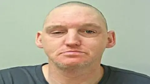 Lancashire Police A police mugshot of a man with closely cropped hair and some grey facial hair. He is wearing a grey T-shirt.