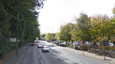 Peel Road is lined with trees as a few cars drive along it.