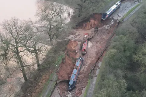 Shropshire Fire & Rescue Service Aerial photo of canal, with two narrowboats lying in a sunken stretch of the canal. A field to the left is covered in water below what looks like a landslip