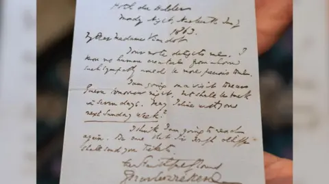 An unseen curator holds up a letter handwritten by the author Charles Dickens.