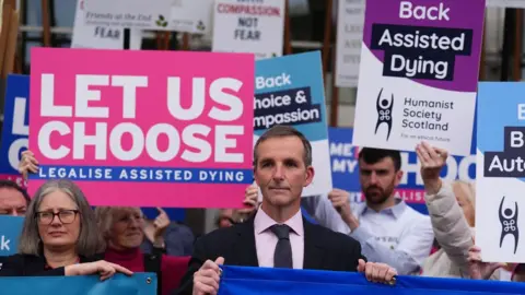 PA Media Liam McArthur stands alongside people holding signs in favour of his assisted dying bill outside the Scottish Parliament