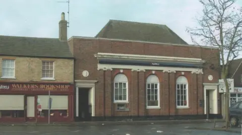 March and District Museum Colour photo from 2005 shows the Georgian style façade of the NatWest building on the right and a book shop called 'Walkers' on the left. You can see a NatWest sign above the three arched windows and imposing doorways at each end of the building.