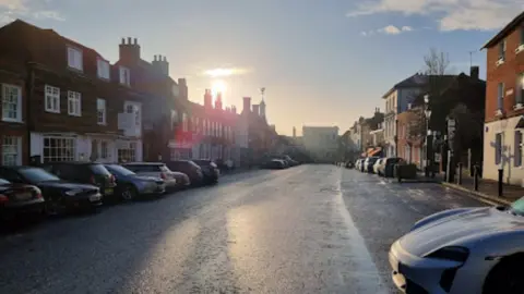 A street view of Castle Street in Farnham Town Centre, Surrey. Bright blue skies, a winter sun and a line of parked cars.