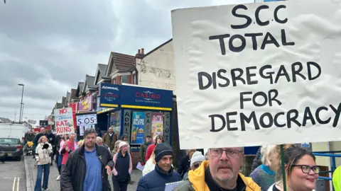 LDRS A group of people walking down the street holding placards and signs opposing the Portswood bus gate scheme.