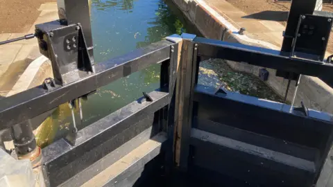 Alex Pope/BBC Black gates in a lock, with water running through the middle. There are constructed walls either side of it. 