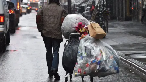 Getty Images Photo shows a man pulling a cart with bags of bottles attached through the street in New York City