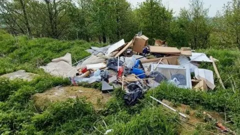 Fly-tipping - a large pile of waste dumped by grass and trees at a beautiful nature spot in Haworth, West Yorkshire