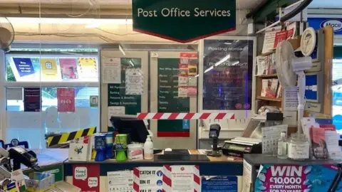 A Post Office desk with colourful posters and a set-up to take payments 