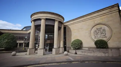 PA Media The High Court in Glasgow, a sandstone building with a circle of columns at the entrance. A large crest is emblazoned on the wall near the entrance.