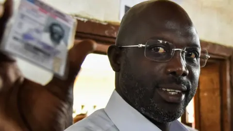 AFP Former football star George Weah shows his voting card at a polling station in Monrovia on October 10, 2017