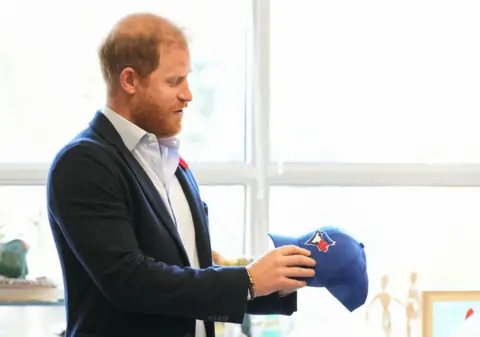 Nathan Denette /The Canadian Press via AP Prince Harry looks at a Toronto Blue Jays hat.
