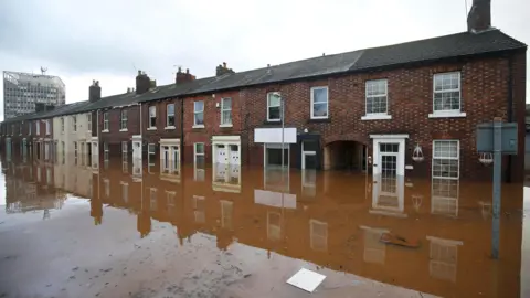 REUTERS/Andrew Yates A row of two-storey red brick terraced houses reflected in brown muddy water that has risen to half way up the front doors