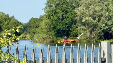Leicester Media Online Police divers are seen in the distance on a lake with trees surrounding the lake.