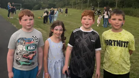 Four children smile at them camera, two have ginger hair the other two have dark hair