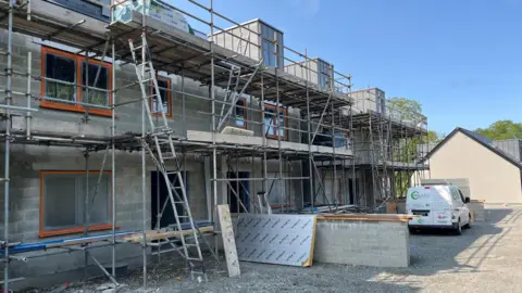 A building site, with scaffolding and partly built houses behind it. 