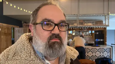 Man with glasses and beard stands in front of a bar
