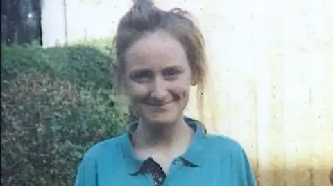 A young woman with light brown hair, wearing a turquoise top, smiles into the camera